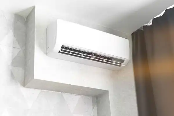 Wall-mounted air conditioning unit installed in a room corner, next to dark curtains.
