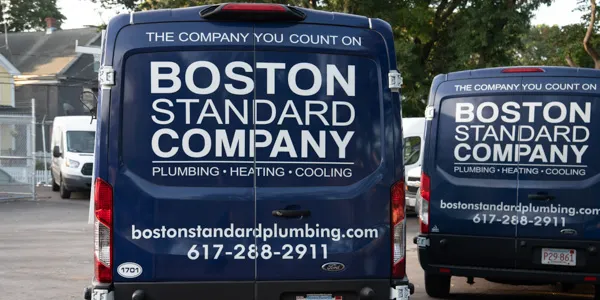 Rear view of two dark blue service vans branded with "Boston Standard Company" and offering plumbing, heating, and cooling services.