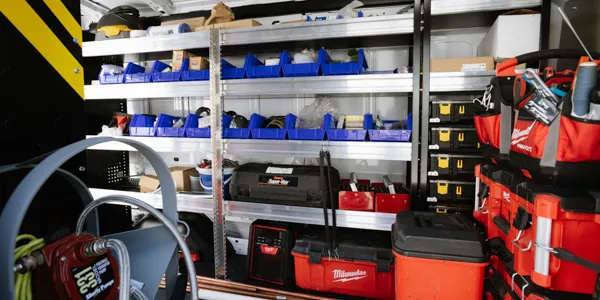 Interior of a service van with organized shelves, blue bins, and red toolboxes filled with tools and equipment.