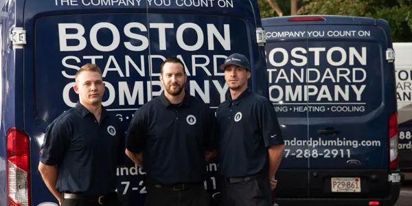 Three men in dark blue uniforms stand in front of two dark blue service vans.